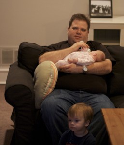 Brenden watches tv while Patrick feeds Emily.